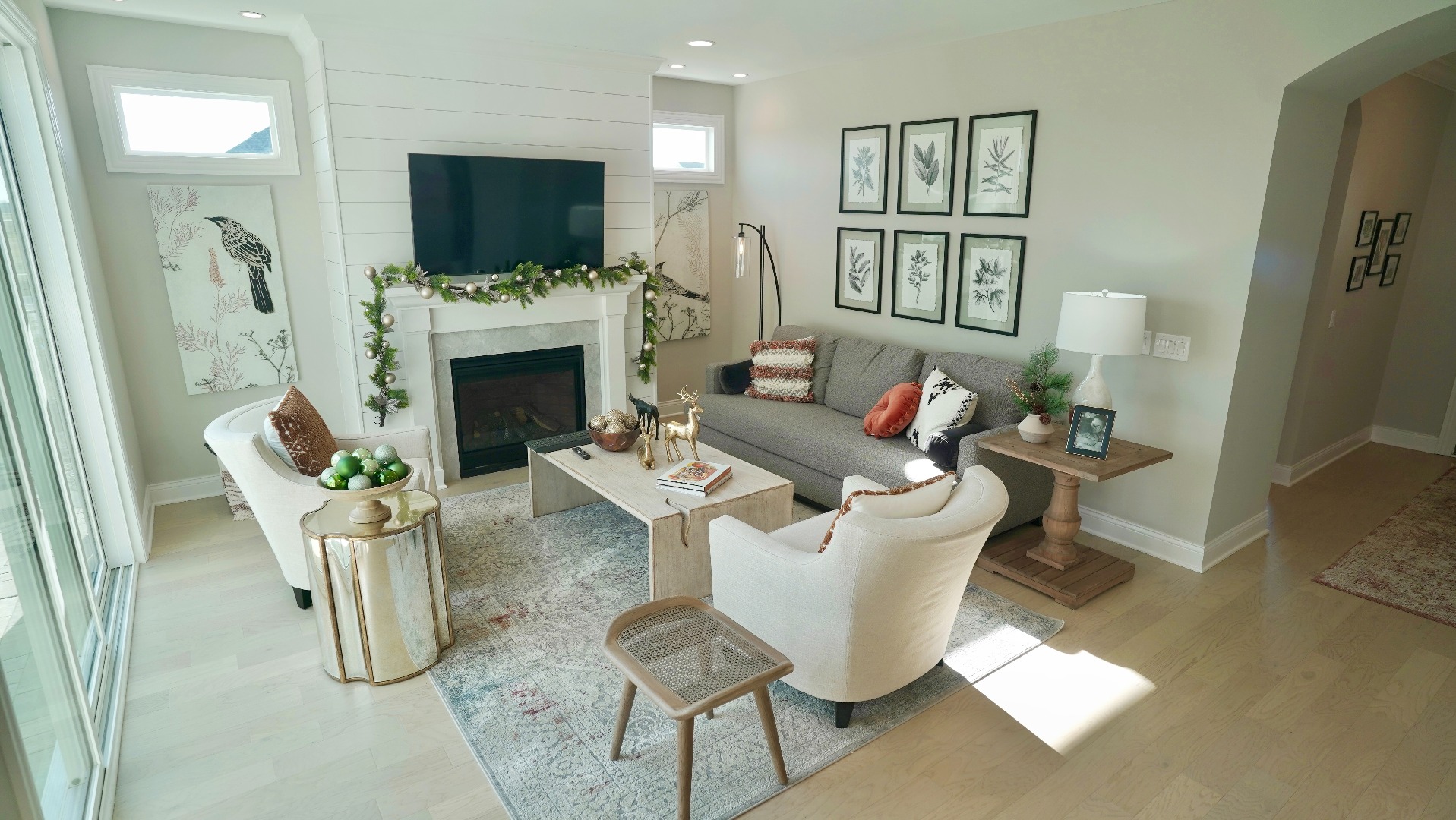 A cozy yet bright living room space featuring subtle winter foliage draped over a fireplace. Light furnishings throughout.